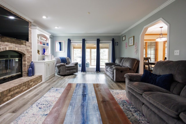 living area featuring a fireplace, ornamental molding, arched walkways, and light wood-style floors