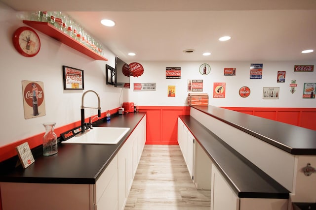 kitchen featuring recessed lighting, light wood finished floors, a sink, a wainscoted wall, and dark countertops