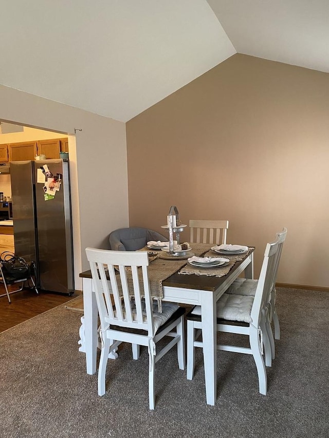 dining space featuring lofted ceiling and dark carpet