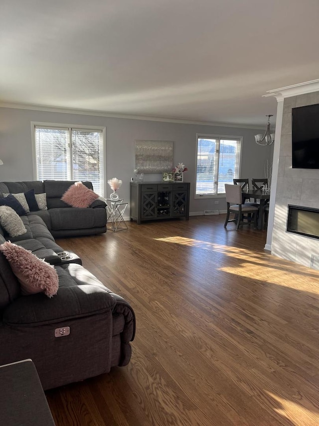 living room with wood finished floors, a tiled fireplace, crown molding, and baseboards