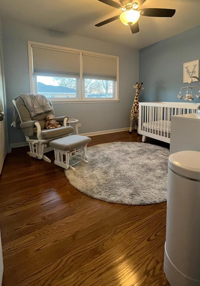 bedroom featuring ceiling fan, a nursery area, wood finished floors, and baseboards