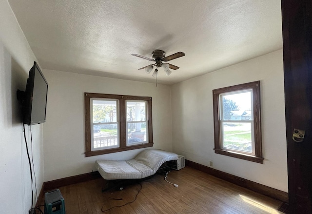 living area with wood finished floors, plenty of natural light, a ceiling fan, and baseboards