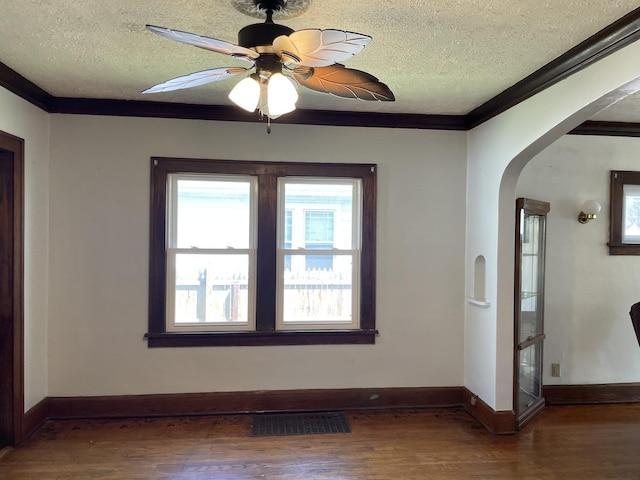 empty room with arched walkways, a textured ceiling, wood finished floors, and ornamental molding