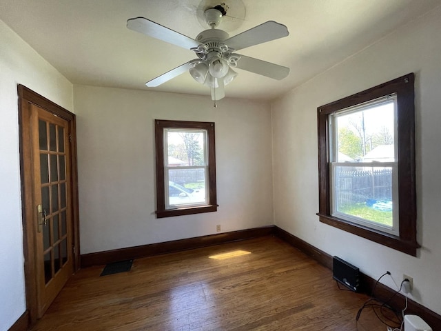 empty room with a wealth of natural light, wood finished floors, visible vents, and baseboards