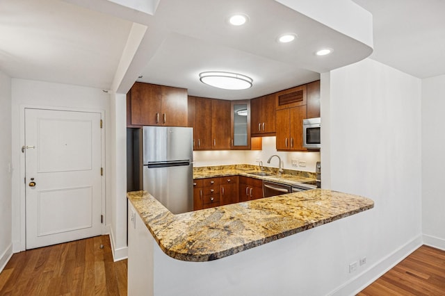 kitchen with appliances with stainless steel finishes, wood finished floors, a peninsula, and baseboards