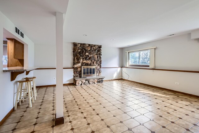 living room featuring a stone fireplace, baseboards, and visible vents