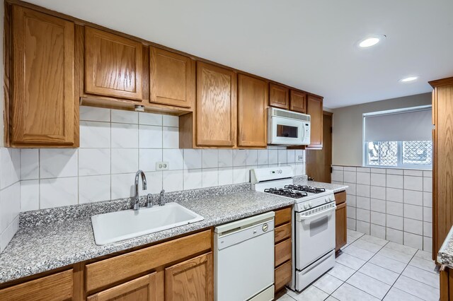 kitchen featuring tile walls, brown cabinets, a sink, light countertops, and white appliances