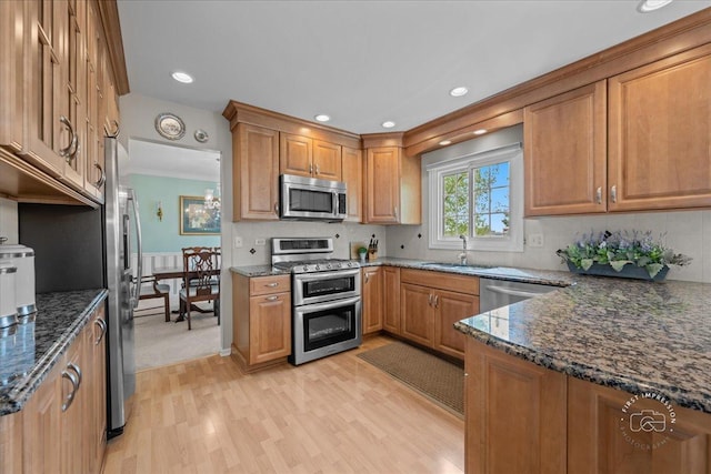 kitchen with light wood-style floors, brown cabinets, a sink, dark stone countertops, and appliances with stainless steel finishes