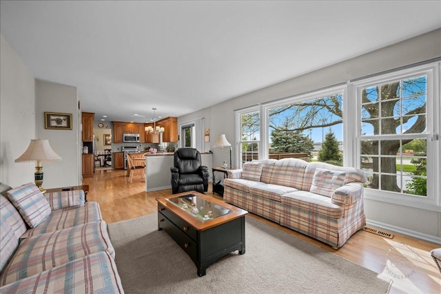 living area with light wood-style floors, baseboards, visible vents, and a notable chandelier