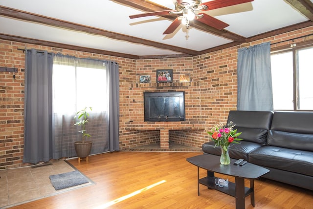 living room featuring beam ceiling, brick wall, a wealth of natural light, and ceiling fan