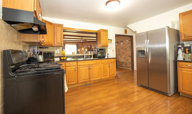 kitchen featuring a sink, stainless steel appliances, under cabinet range hood, light wood-style flooring, and dark countertops