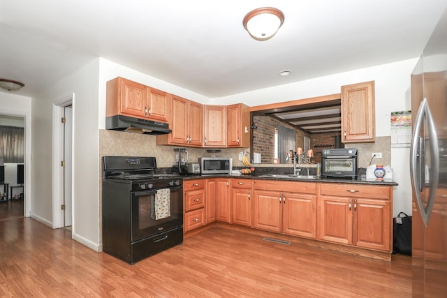 kitchen featuring stainless steel microwave, a sink, under cabinet range hood, light wood-style floors, and gas stove