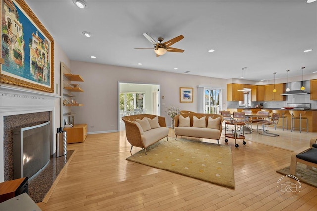 living room with recessed lighting, a fireplace with flush hearth, light wood-style flooring, and a ceiling fan
