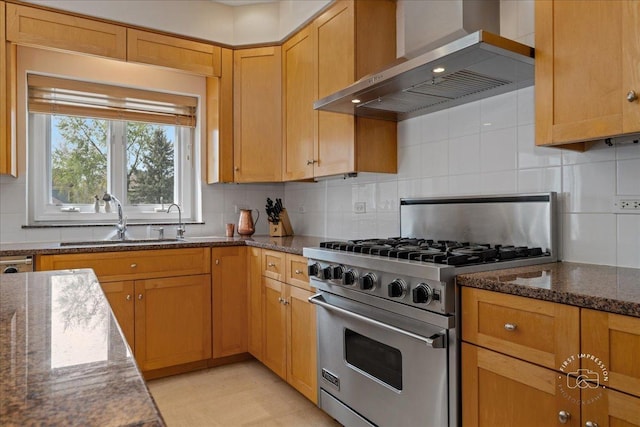 kitchen with wall chimney range hood, a sink, dark stone countertops, high end stove, and backsplash