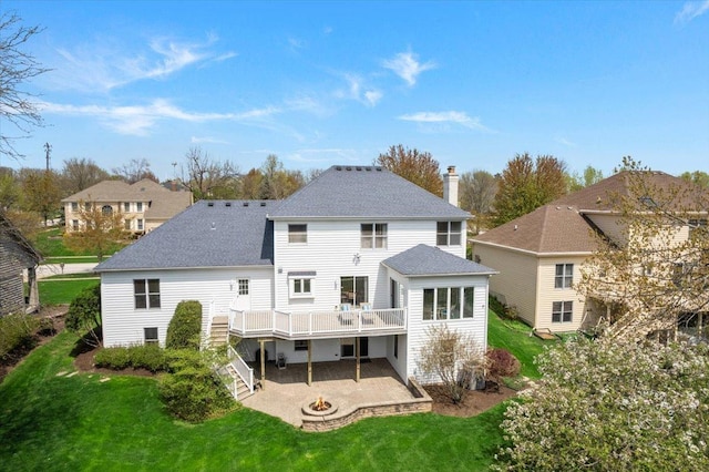 back of property with roof with shingles, an outdoor fire pit, a wooden deck, a lawn, and a patio