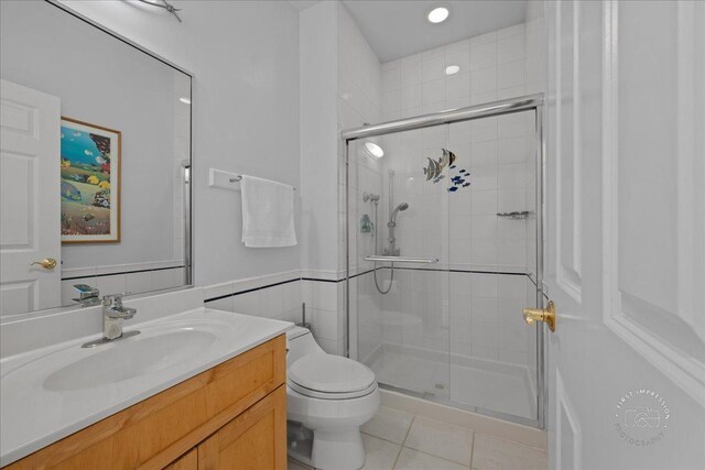 full bath with tile patterned flooring, vanity, toilet, a wainscoted wall, and a stall shower