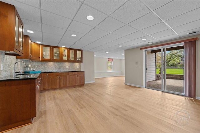 kitchen with brown cabinetry, dark countertops, light wood-style floors, baseboards, and a sink