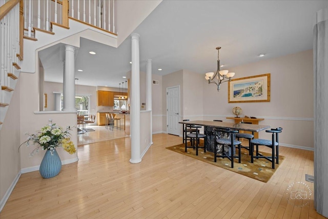 dining area featuring ornate columns, baseboards, light wood finished floors, and stairs