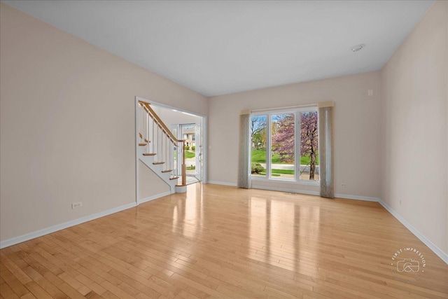 unfurnished room featuring stairway, baseboards, and light wood-style floors