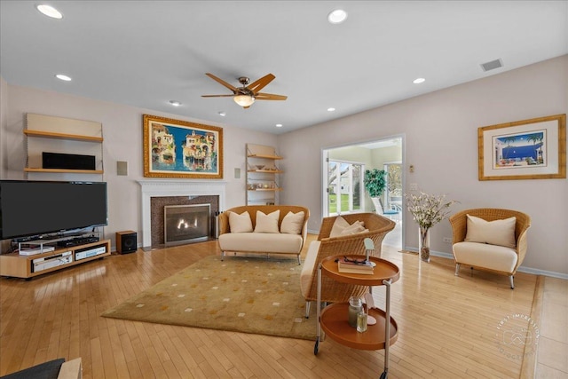 living area with wood-type flooring, visible vents, baseboards, a ceiling fan, and a premium fireplace