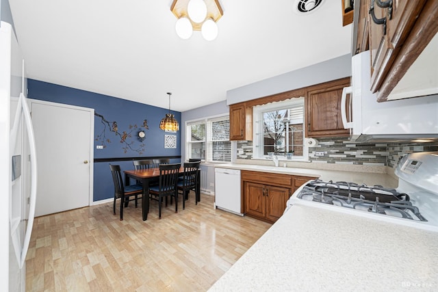 kitchen with white appliances, brown cabinetry, light countertops, light wood-type flooring, and wainscoting