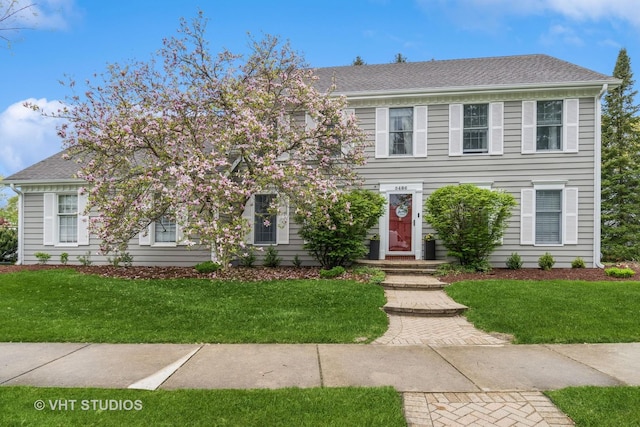 colonial inspired home featuring a shingled roof and a front lawn