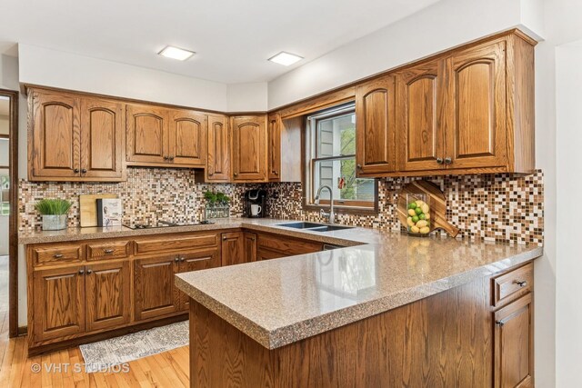 kitchen with brown cabinetry, a peninsula, tasteful backsplash, a sink, and light wood finished floors