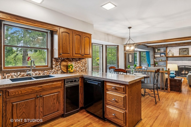 kitchen featuring brown cabinets, a sink, black dishwasher, a peninsula, and decorative backsplash