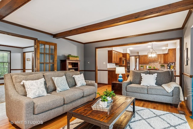 living area with an inviting chandelier, ornamental molding, light wood finished floors, and beamed ceiling