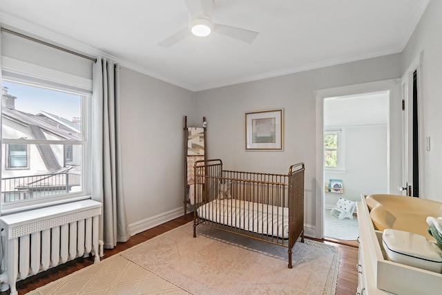 bedroom featuring ornamental molding, radiator, wood finished floors, baseboards, and a nursery area