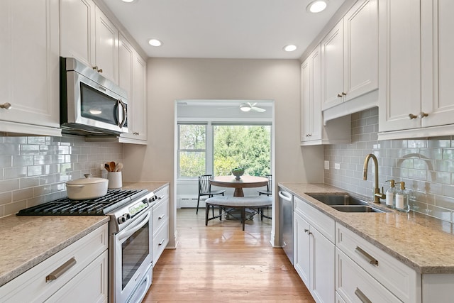 kitchen featuring appliances with stainless steel finishes, a sink, light wood finished floors, and tasteful backsplash