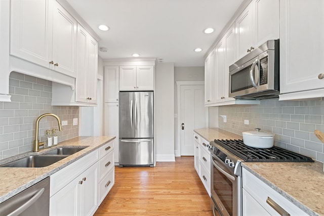kitchen with backsplash, appliances with stainless steel finishes, a sink, and light wood finished floors