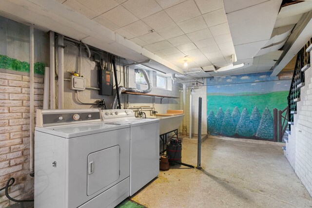laundry area featuring laundry area, electric panel, brick wall, and separate washer and dryer