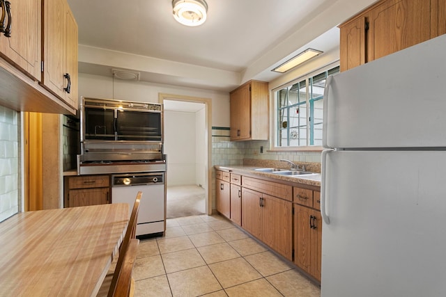 kitchen featuring a sink, white appliances, light countertops, light tile patterned floors, and tasteful backsplash