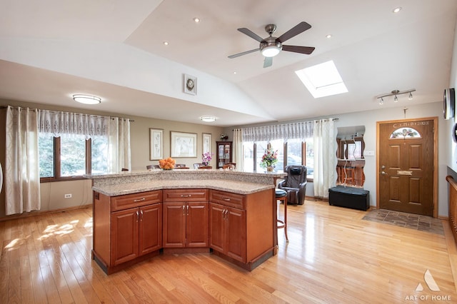 kitchen featuring a breakfast bar, ceiling fan, a kitchen island, light wood-style floors, and lofted ceiling with skylight