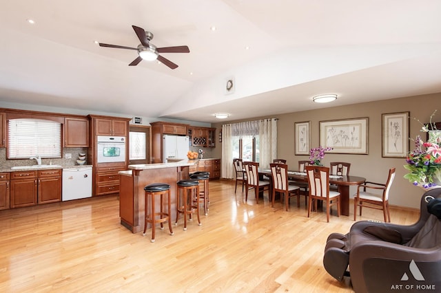 kitchen with brown cabinets, a kitchen breakfast bar, a ceiling fan, vaulted ceiling, and white appliances