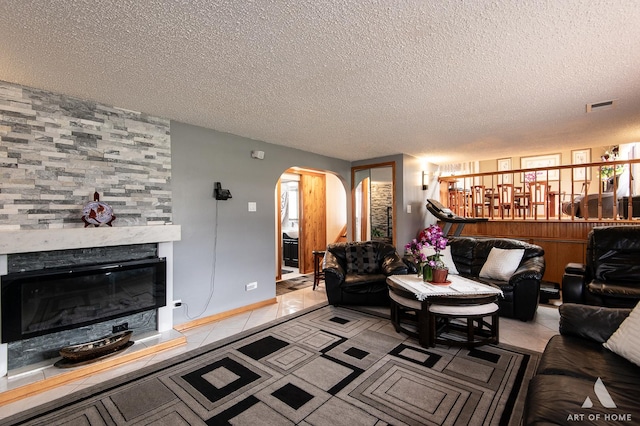 living area with arched walkways, light tile patterned floors, a stone fireplace, visible vents, and a textured ceiling