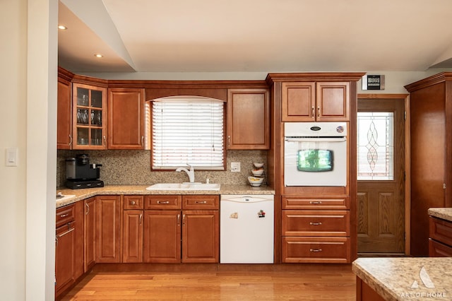 kitchen featuring decorative backsplash, a sink, light wood finished floors, vaulted ceiling, and white appliances