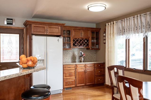 bar with white fridge with ice dispenser, backsplash, light wood finished floors, and plenty of natural light
