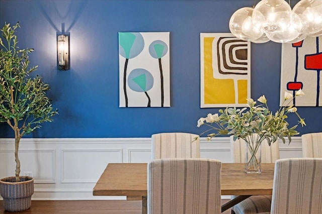 dining area featuring an inviting chandelier, a wainscoted wall, a decorative wall, and wood finished floors