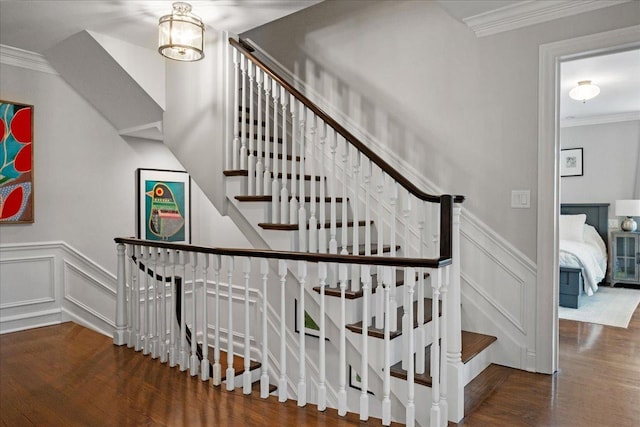 staircase featuring a wainscoted wall, ornamental molding, a decorative wall, and wood finished floors