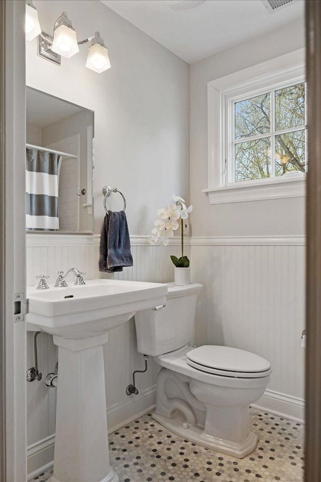full bath with toilet, a wainscoted wall, baseboards, curtained shower, and visible vents