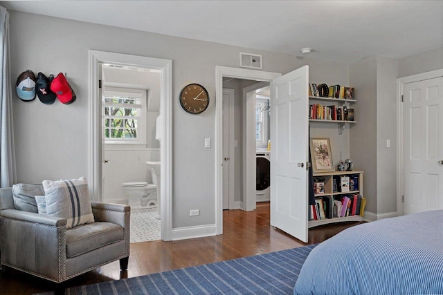 bedroom featuring baseboards, ensuite bath, wood finished floors, and visible vents