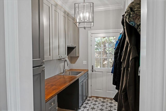 laundry room with an inviting chandelier, ornamental molding, a sink, and light floors
