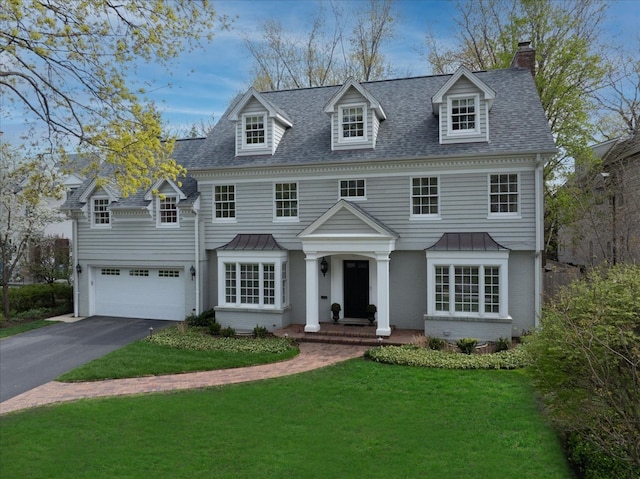 view of front of house with a shingled roof, a front lawn, a garage, a chimney, and driveway