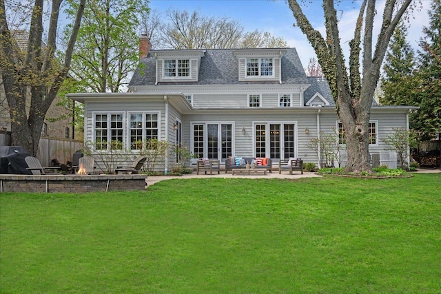 back of property with a lawn, an outdoor living space with a fire pit, a chimney, and a patio