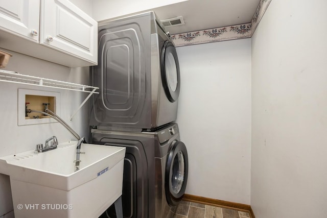 laundry area featuring stacked washer / dryer, cabinet space, wood finished floors, a sink, and baseboards