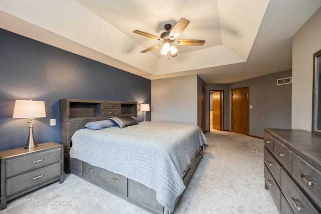 bedroom with a tray ceiling, visible vents, light carpet, and ceiling fan