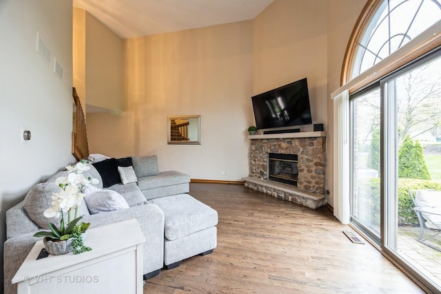 living room with high vaulted ceiling, visible vents, a stone fireplace, and wood finished floors