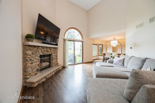 living room with a stone fireplace, visible vents, wood finished floors, baseboards, and a high ceiling